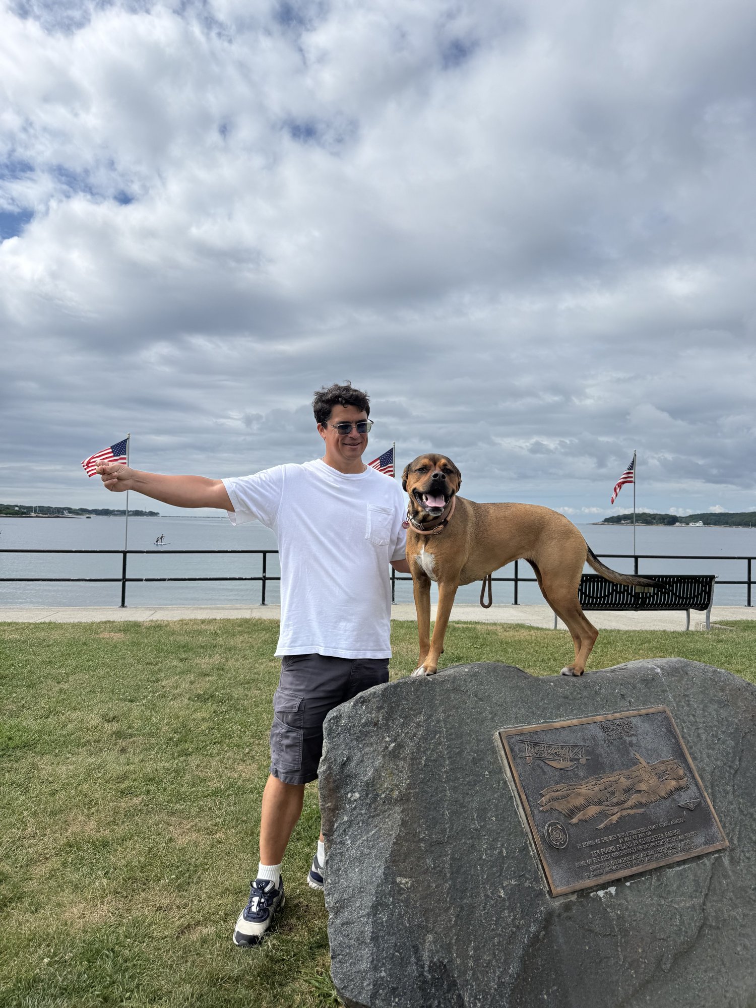 Calder and Rosie on a granite boulder by the harbor, flags behind them