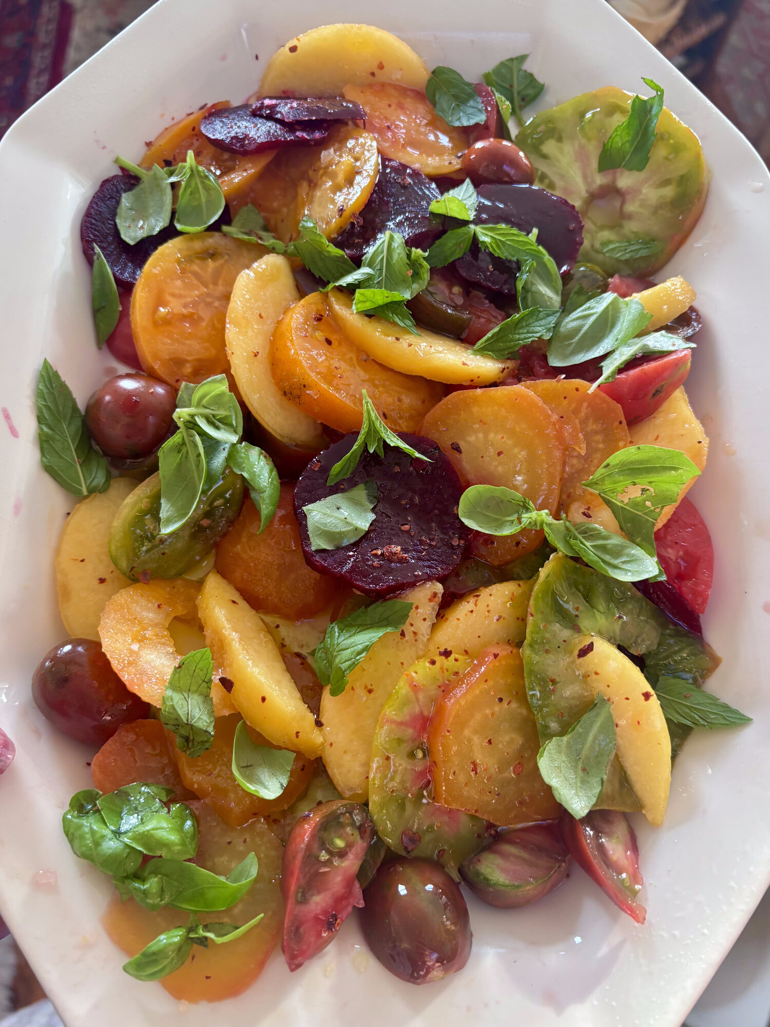 Platter of sliced tomatoes, beets and peaches with fresh basil and mint, dressed with olive oil