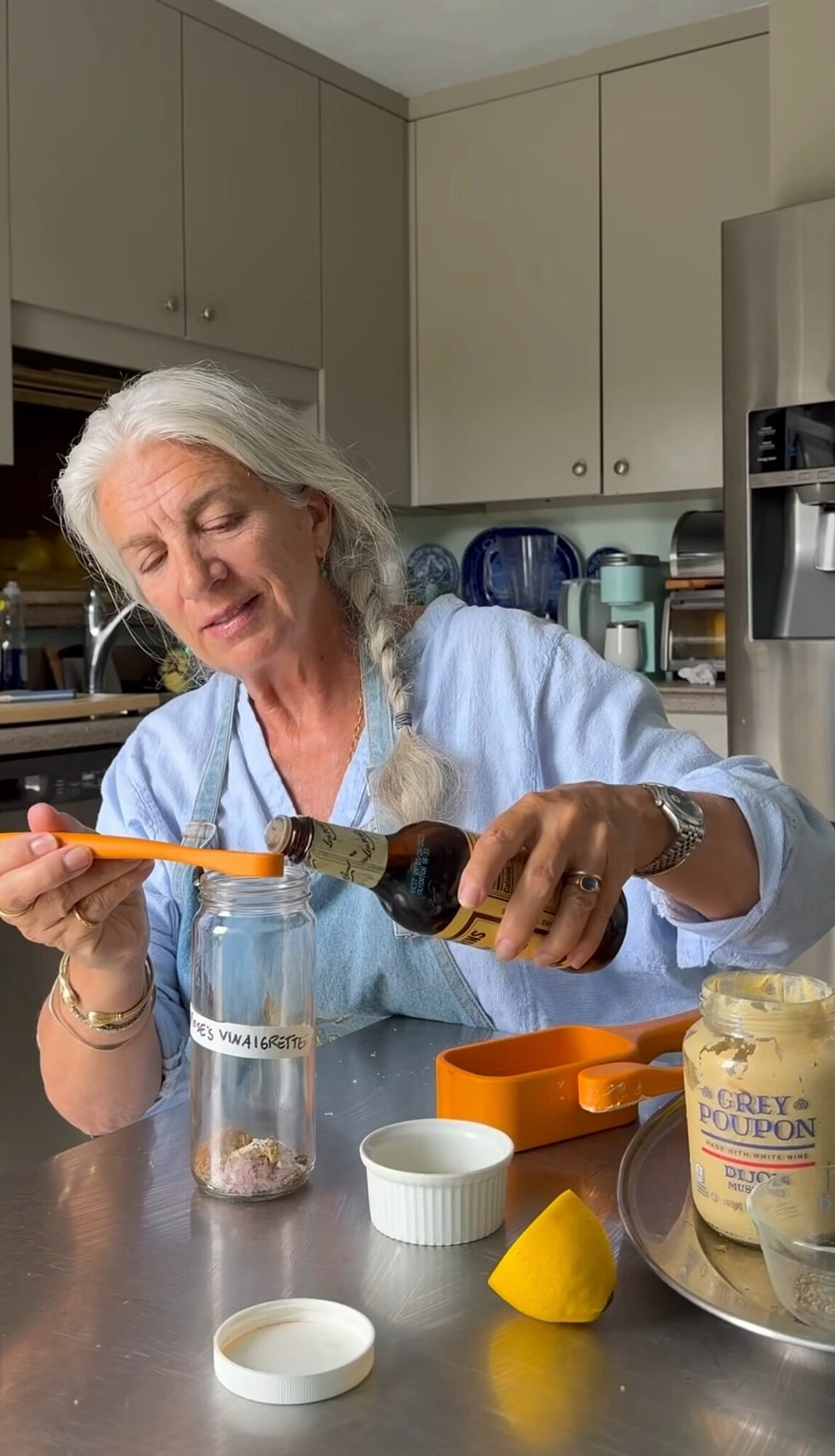 Lucinda Scala Quinn pouring Worcestershire sauce into a glass jar labeled Rose's Vinaigrette, with Mad Hungry measuring spoons and Dijon mustard on the counter